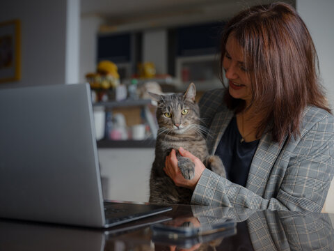 Mother working remotely from home, caucasian woman with her cat using laptop at home. Smart working and smart studying with pet