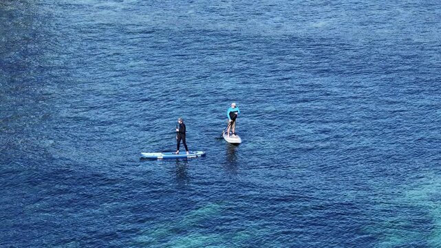 Two People Stand Up Paddleboarding on Clear Blue Ocean Water