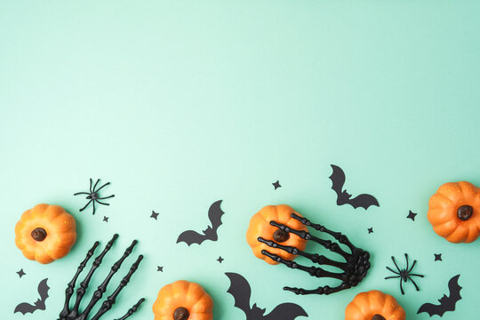 Skeleton hand holding pumpkin with bats and spiders on teal background for Halloween decor.