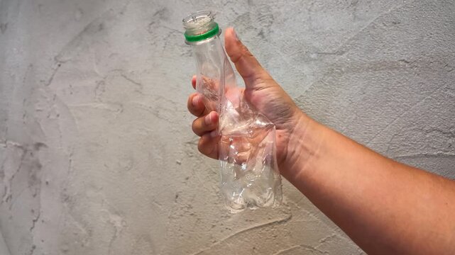 Person Crushing Plastic Water Bottle for Recycling Against Concrete Wall