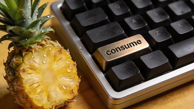 Custom-made premium keyboard with the key "consume" and a freshly grown pineapple placed next to the keyboard
