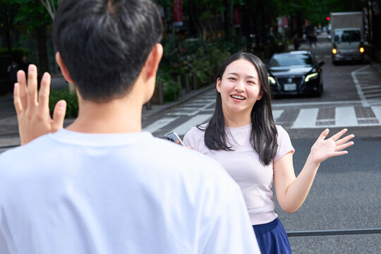 Young Japanese Man and Woman Waving and Greeting Each Other on City Street
