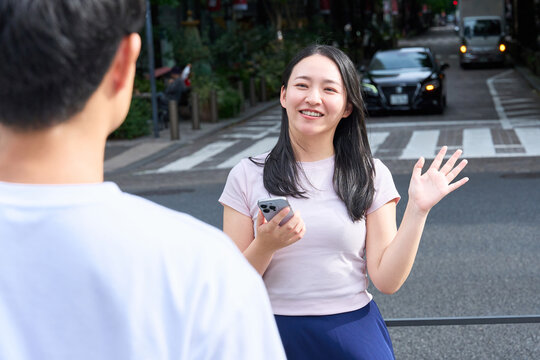 Young Japanese Man and Woman Waving and Greeting Each Other on City Street