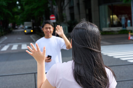 Young Japanese Man and Woman Waving and Greeting Each Other on City Street