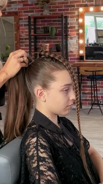 Stylist secures long hair into an elegant braided ponytail in a salon, professional hairstyling, beauty transformation, polished youthful look.