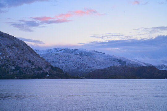 Snow-covered mountain range by a calm fjord at twilight