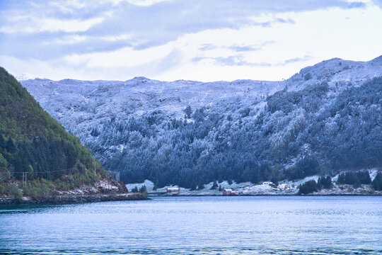 Snow-covered mountain slopes and small huts by a Nordic fjord