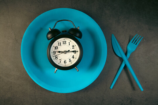Alarm clock on blue plate with fork and knife on dark background
