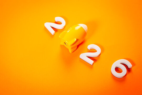 New year 2026 is coming concept. Toy piggy bank on orange background.