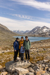 Fototapeta premium Beautiful european family with children and pet dog, hiking Kyrkja mountain on a beautiful sunny summer day, sunset, snow, lakes, valley