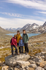 Fototapeta premium Beautiful european family with children and pet dog, hiking Kyrkja mountain on a beautiful sunny summer day, sunset, snow, lakes, valley