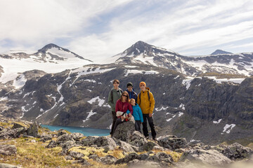 Fototapeta premium Beautiful european family with children and pet dog, hiking Kyrkja mountain on a beautiful sunny summer day, sunset, snow, lakes, valley