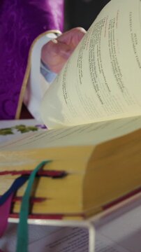 Priest in a purple vestment, a chasuble, turning pages in a Missal, a liturgical book of the Eucharistic prayer during Catholic Mass.