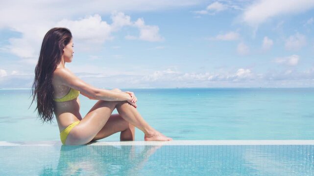 Spa body wellness therapy Asian beauty swimsuit model woman on luxury pampering pool resort relaxing sunbathing, sun tan skincare. Raw unedited video of real unretouched woman without makeup