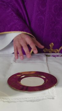 Catholic priest leading the Eucharist Liturgy, reading from the liturgical book placed on the altar with sacred vessels, chalice, and paten.