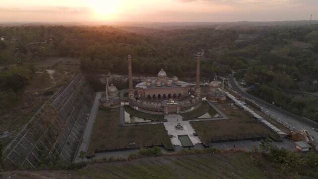 Aerial view of Masjid Samin Baitul Muttaqin at sunset with surrounding hills and lush greenery in Bojonegoro, East Java, Indonesia.