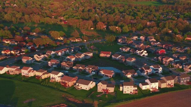 Golden hour drone view of a residential subdivision in DeForest, Wisconsin, with curving streets and homes around a small pond framed by trees and open farmland.