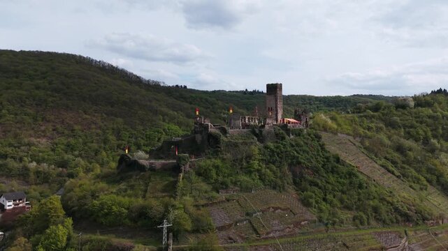 Stunning aerial view with a push forward revealing the majestic Cochem Castle ruins on a verdant hillside in Germany.