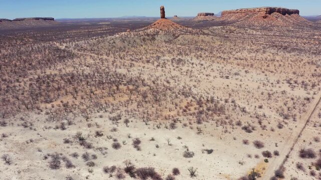 Drone shot of Ugab Valley arid desert landscape reveals The Vingerklip rock formation in background from the west