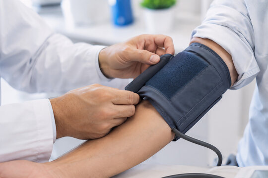 healthcare photo showing only a medical professional's hands placing and adjusting a blood pressure cuff on a patient's arm, white coat sleeve, modern clinic environment