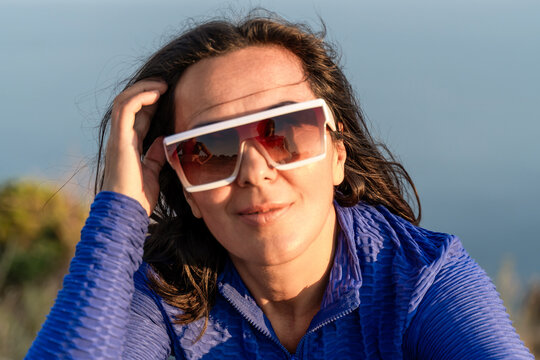 Woman sunglasses portrait wearing blue jacket standing outdoors in sunny golden hour light with reflections in eyewear lenses