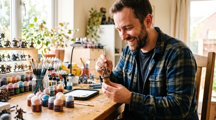 Fototapeta premium Man happily painting miniature figures at a table filled with paints and brushes