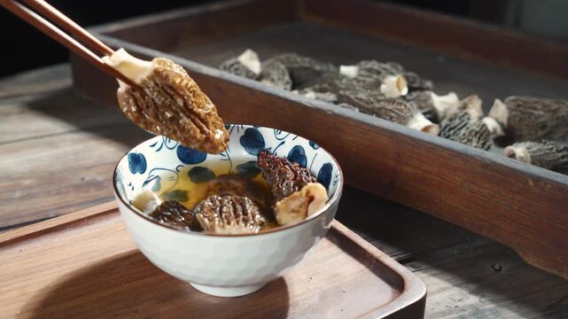 Close Up of Chopsticks Picking Morel Mushroom in Ceramic Bowl