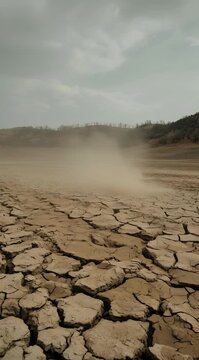 Small dust devil swirling over cracked dry earth landscape, climate change impact, drought effects, environmental disaster, arid ground