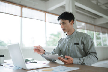 Fototapeta premium Young professional analyzing business charts while working on a laptop in a modern office, representing data analysis, business planning and project management.
