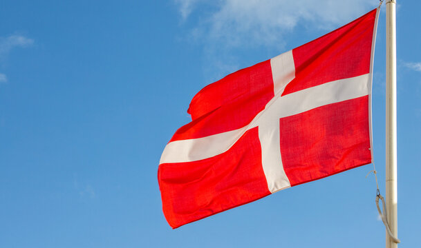 Danish national flag waving on pole against clear blue sky background