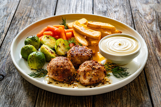 Fried pork meatballs with French fries, mini carrots and brussels sprouts on wooden table
