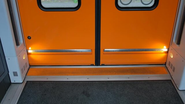 An interior view of the closing automatic door of a modern passenger train onto a paved station platform with an extended safety step.