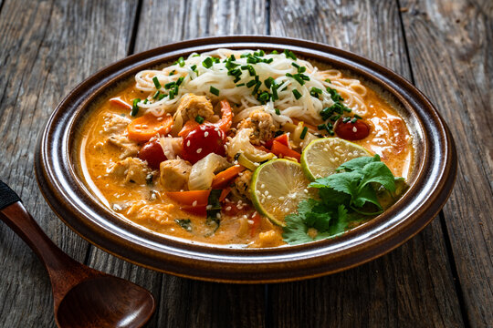 Tom Yum soup - Thai soup with chicken breast nuggets, vegetables and rice noodles on wooden table
