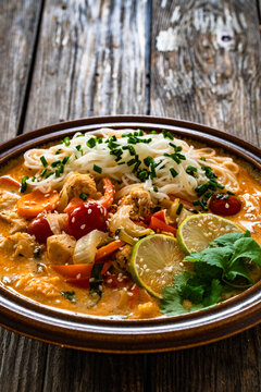 Tom Yum soup - Thai soup with chicken breast nuggets, vegetables and rice noodles on wooden table
