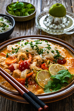 Tom Yum soup - Thai soup with chicken breast nuggets, vegetables and rice noodles on wooden table
