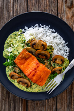 Fried salmon steak with creamy mushroom sauce and white rice on wooden table. Top view
