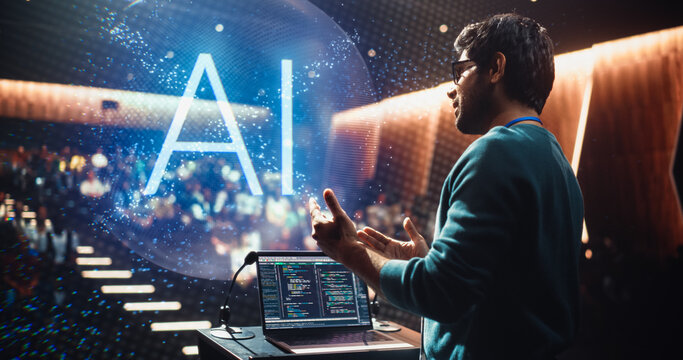 Male Lecturer Delivering a Computer Science AI Keynote From a University Podium, Gesturing to Activate Hologram. Laptop Code SHows as the Auditorium Audience Follows Machine Learning Software Concepts