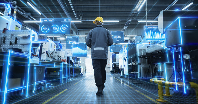 Rear View of an African American Male Worker Walking Between Machines in a Digitalized Factory as Glowing Holographic Panels Display Line Efficiency Percentages, Bar Graphs and Ai Diagnostic Scans.