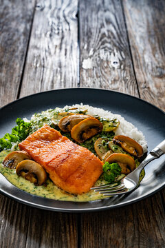 Fried salmon steak with creamy mushroom sauce and white rice on wooden table
