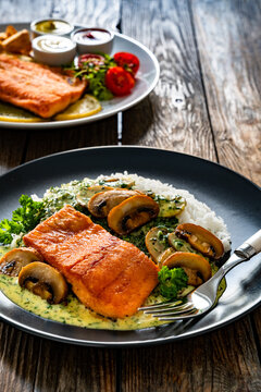 Fried salmon steak with creamy mushroom sauce and white rice on wooden table
