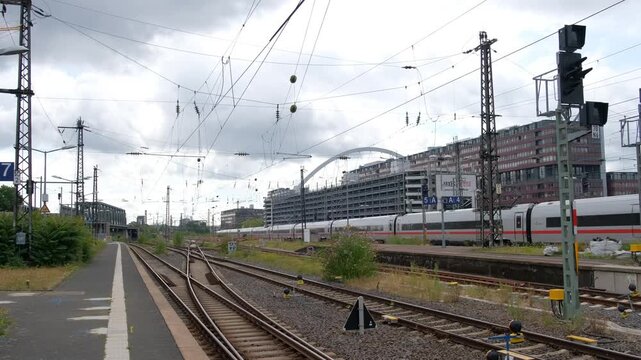 Germany, Cologne-Messe,Deutz, July 25 2025. An expansive view of a long white express train moving through a large railroad junction with overhead electric power lines.