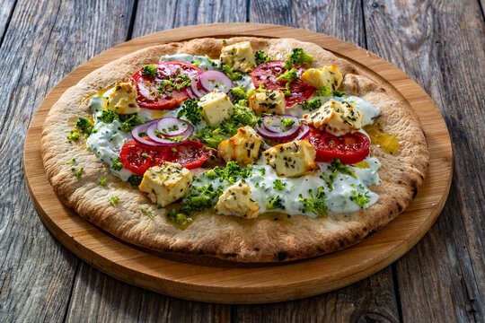 Vegetarian pizza with feta cheese, tomatoes, red onion and broccoli dip on wooden table
