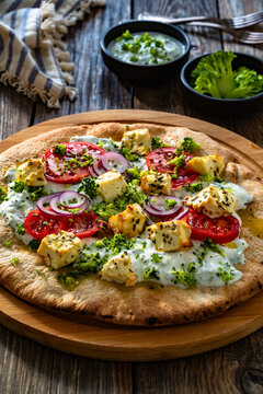 Vegetarian pizza with feta cheese, tomatoes, red onion and broccoli dip on wooden table
