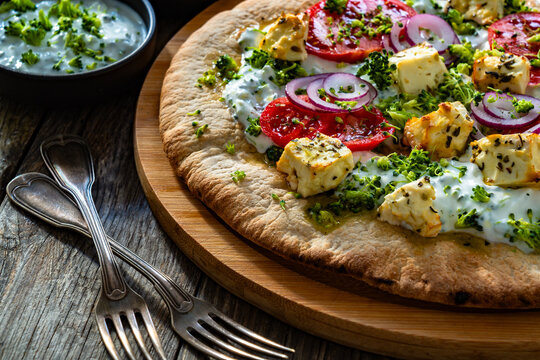 Vegetarian pizza with feta cheese, tomatoes, red onion and broccoli dip on wooden table
