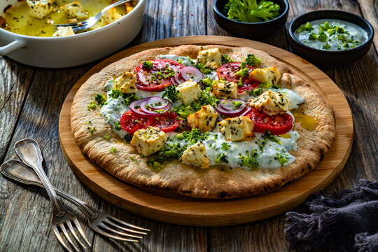 Vegetarian pizza with feta cheese, tomatoes, red onion and broccoli dip on wooden table
