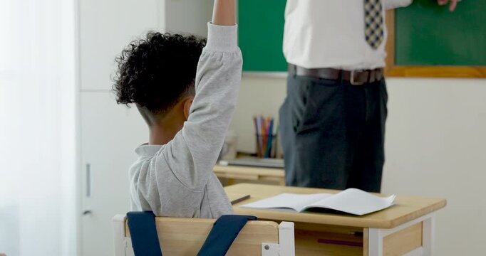 Young boy student sits at wooden desk with open notebook, raises pencil toward male teacher for classroom answer, building confidence during primary lesson, homework practice and participation