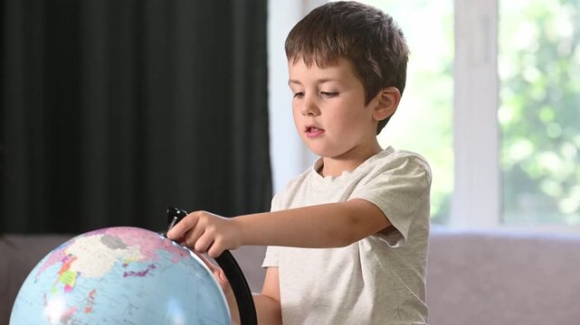 boy studies a globe and looks at a world map at home at the table. Early preschool development. Citizens of the world, a world without borders, globalization.