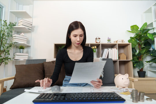 Asian woman using calculator and reviewing tax documents at home workspace