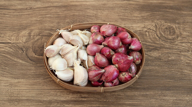 Garlic cloves and red onion or shallots on woven bamboo plate. Top view
