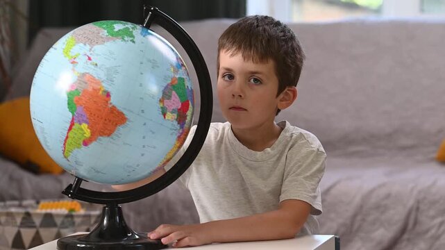 A child studies a globe and looks at a world map at home at the table. Early preschool development. Citizens of the world, a world without borders, globalization.